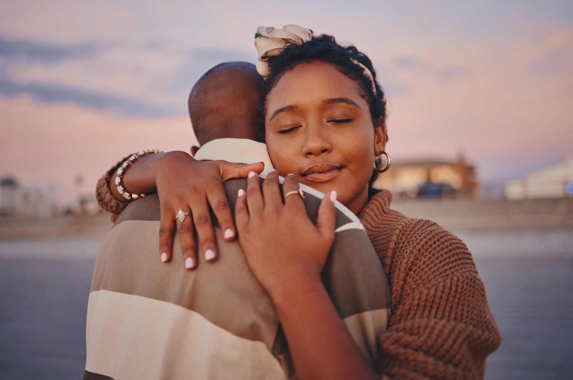 A close-up of a woman embracing a man outdoors at sunset.