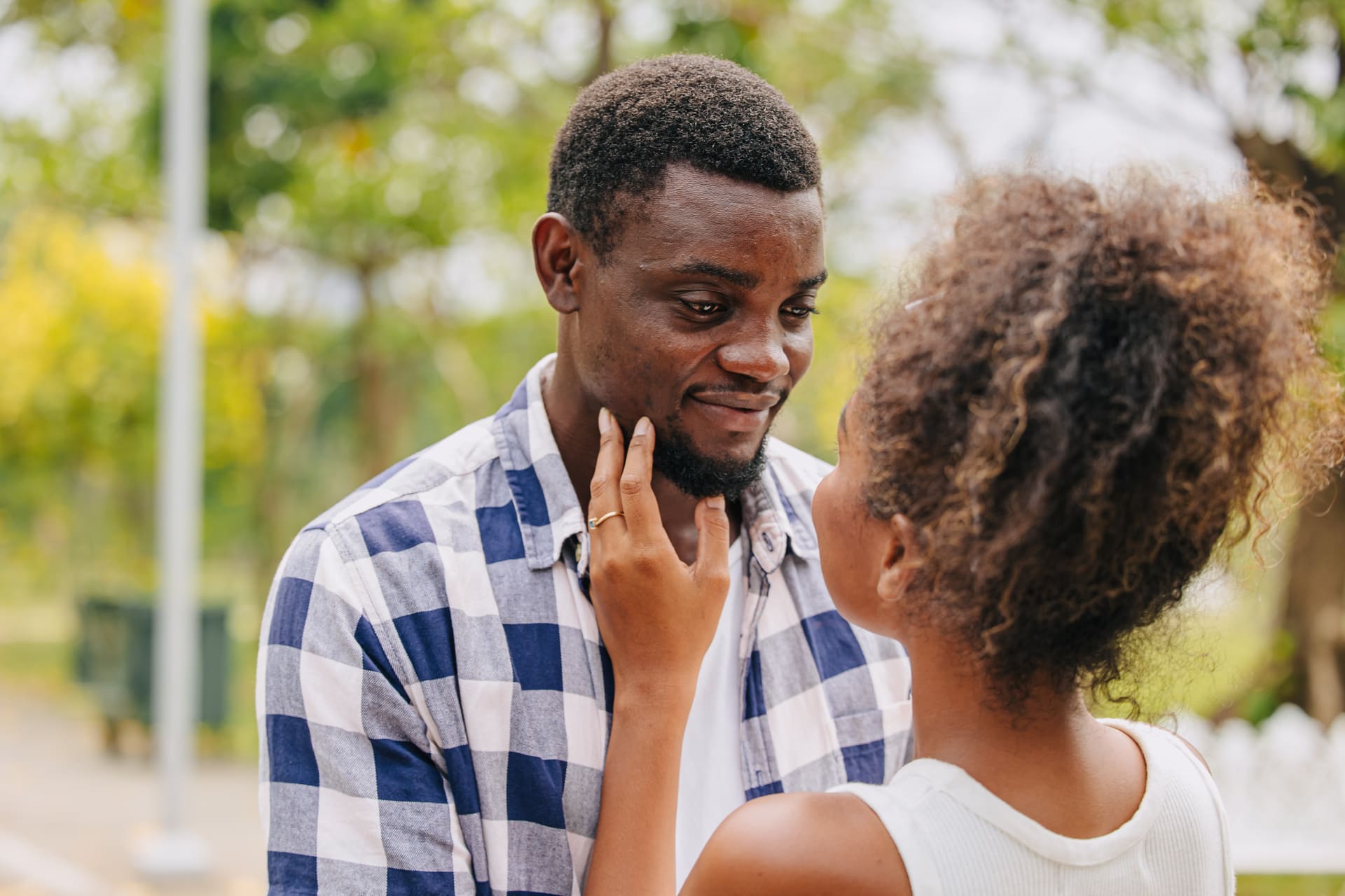 A woman gently touches a smiling man's face outdoors.