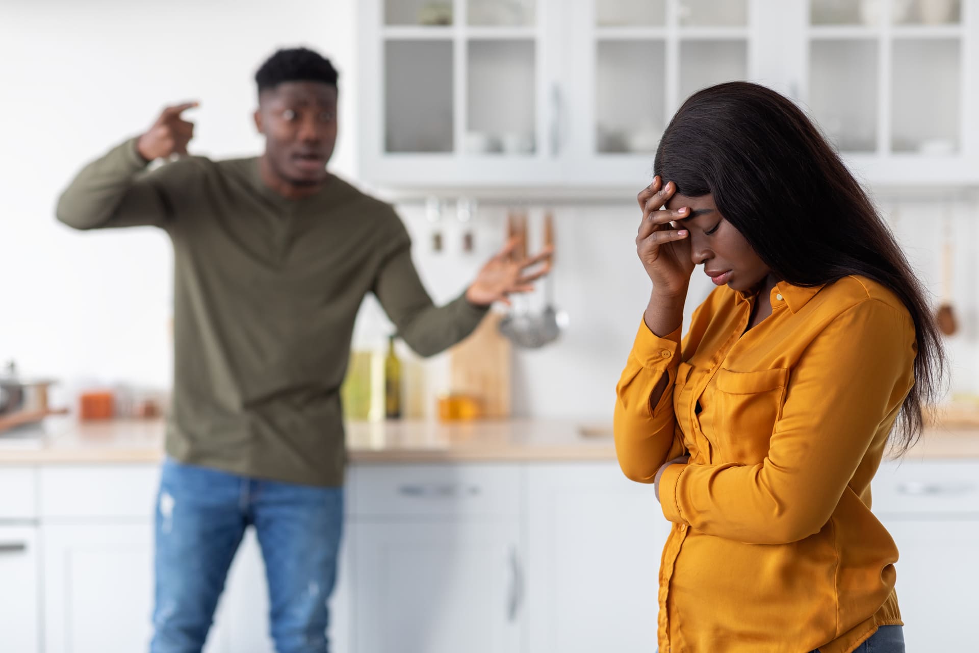 A man angrily gesturing at a woman who looks upset in a kitchen.