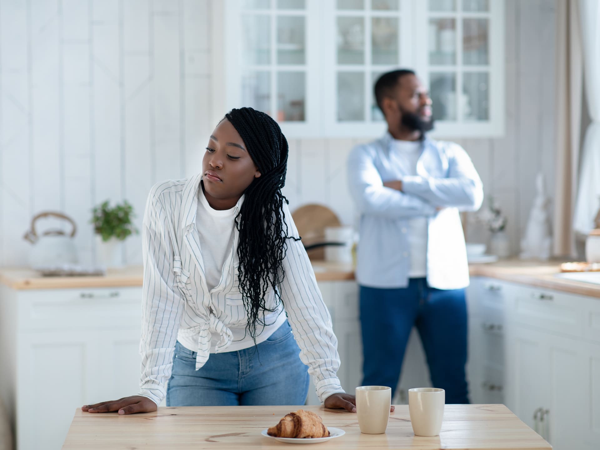 A woman looking away while a man stands with arms crossed in the background.